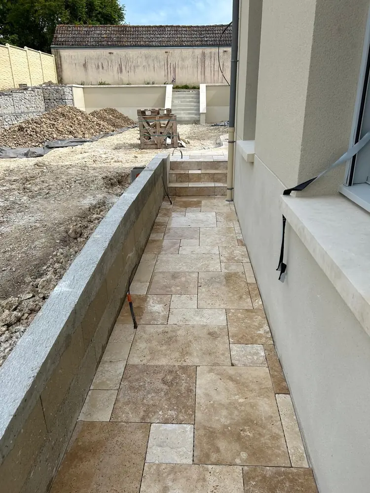 Allée en travertin posé en opus le long d'une maison neuve, entre façade et muret de soutènement