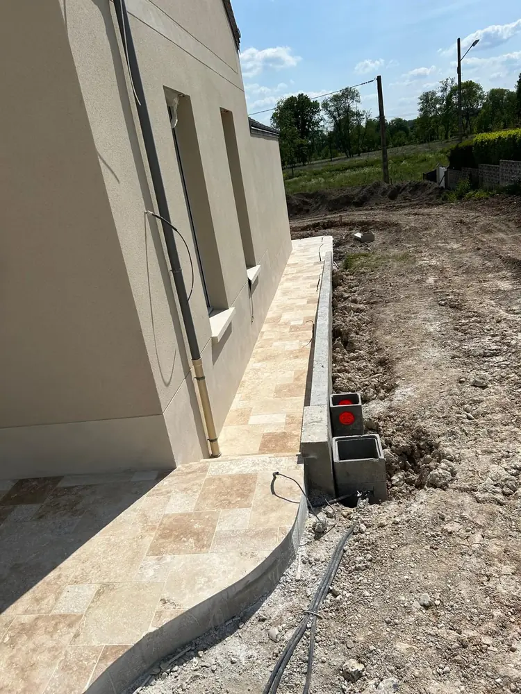 Terrasse en travertin opus à bordure courbe longeant la façade d'une maison neuve