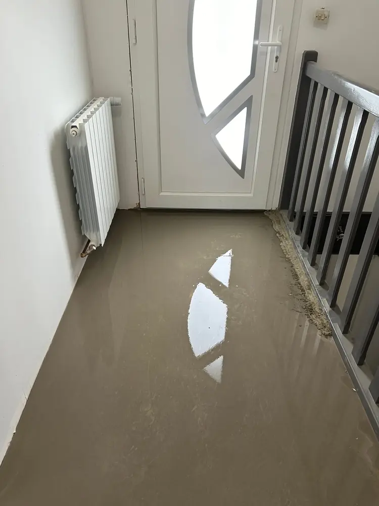 Chape liquide fraîchement coulée dans une entrée, jusqu'au pied de la porte et de l'escalier