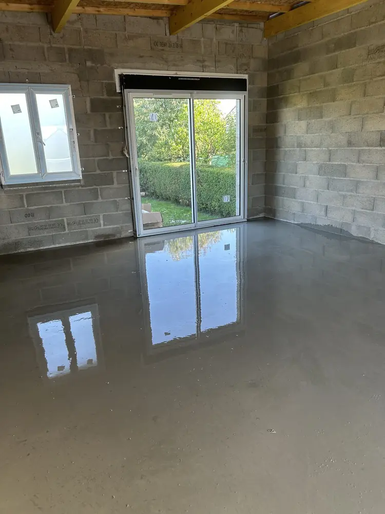 Chape liquide fraîchement coulée dans une extension en parpaing, reflet de la baie vitrée