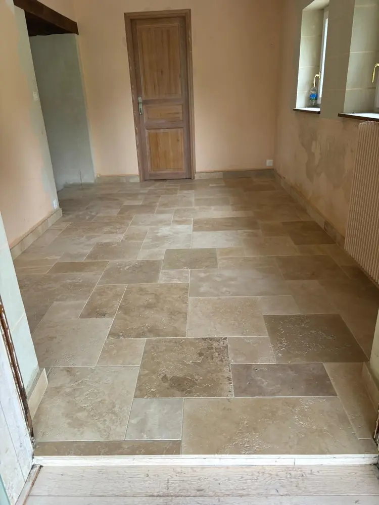 Couloir en travertin opus beige menant à une porte en bois dans une maison ancienne