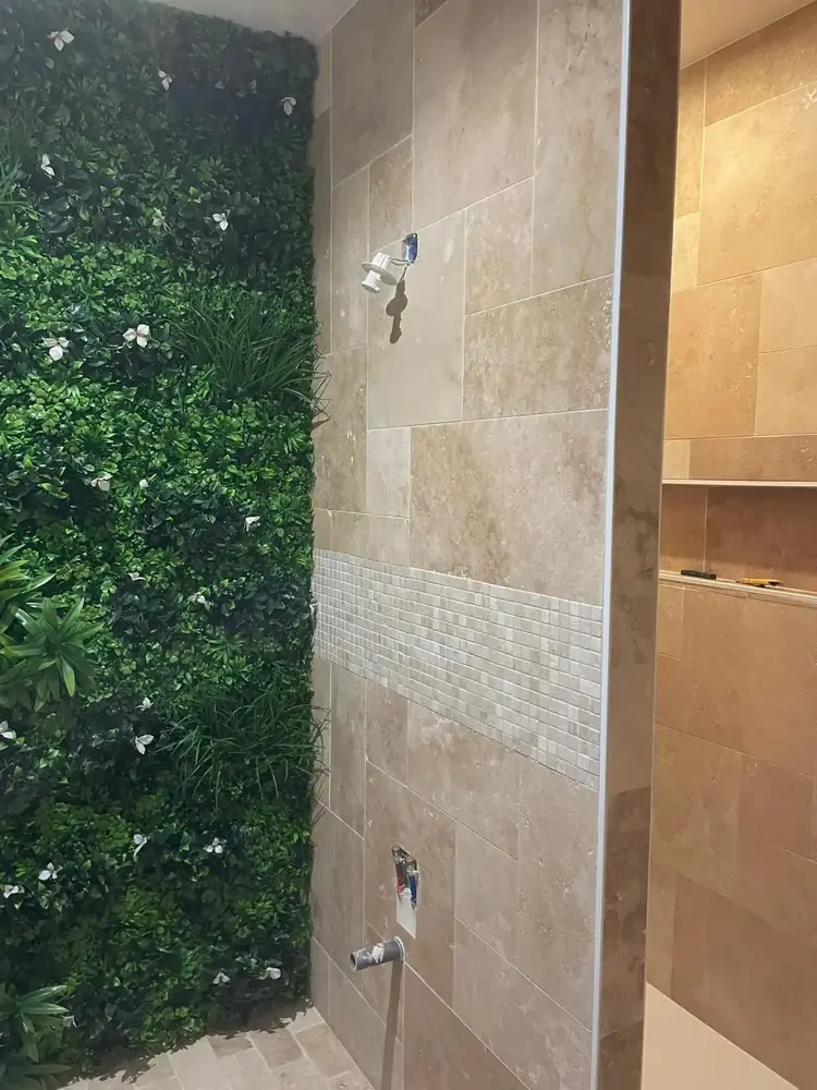 Douche en travertin beige avec frise en mosaïque de travertin à côté d'un mur végétal