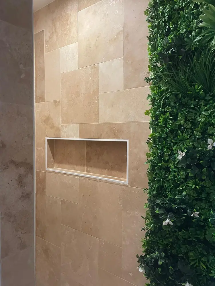 Mur de douche en travertin beige avec niche encastrée, à côté d'un mur végétal