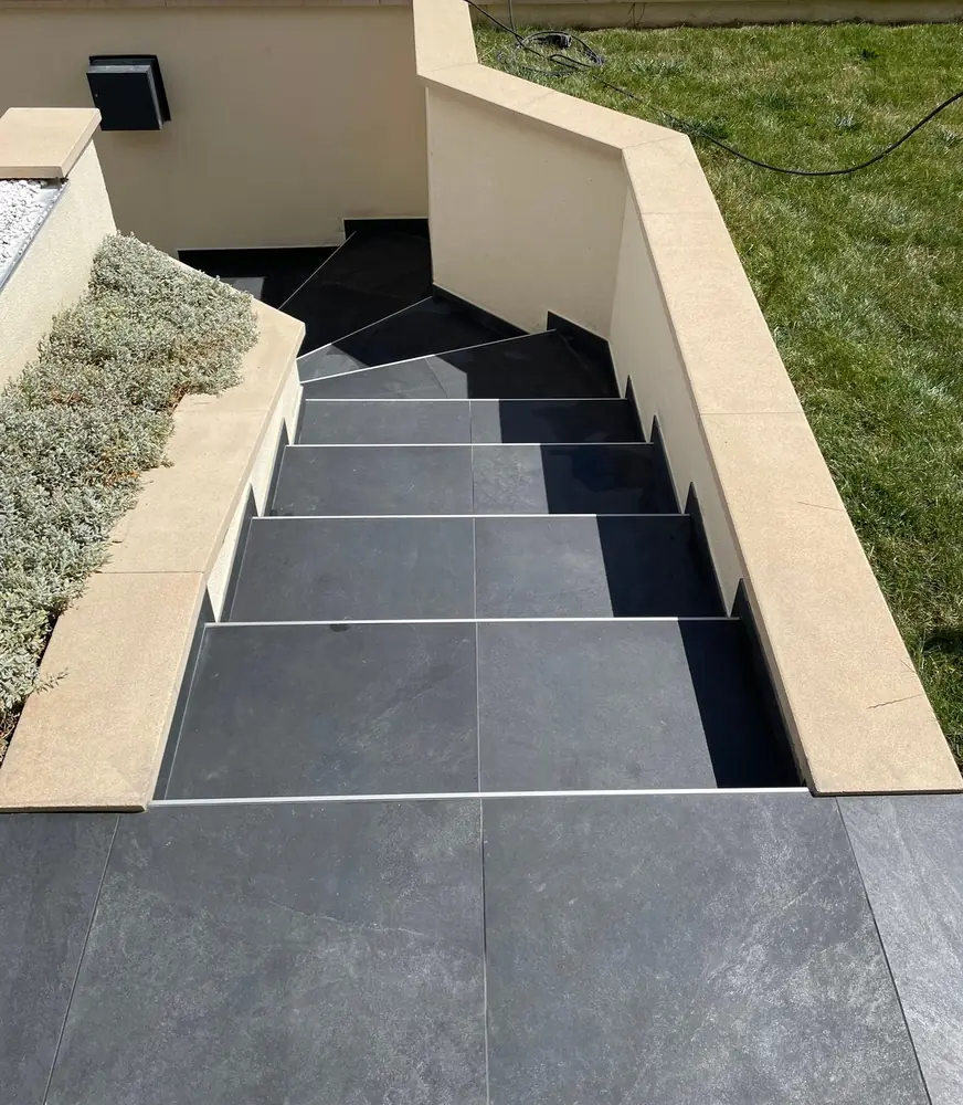 Escalier extérieur en grès anthracite entre deux murets crème, vu depuis le palier