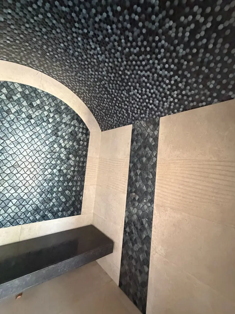 Hammam en mosaïque sombre et grès beige rainuré, banc en pierre noire