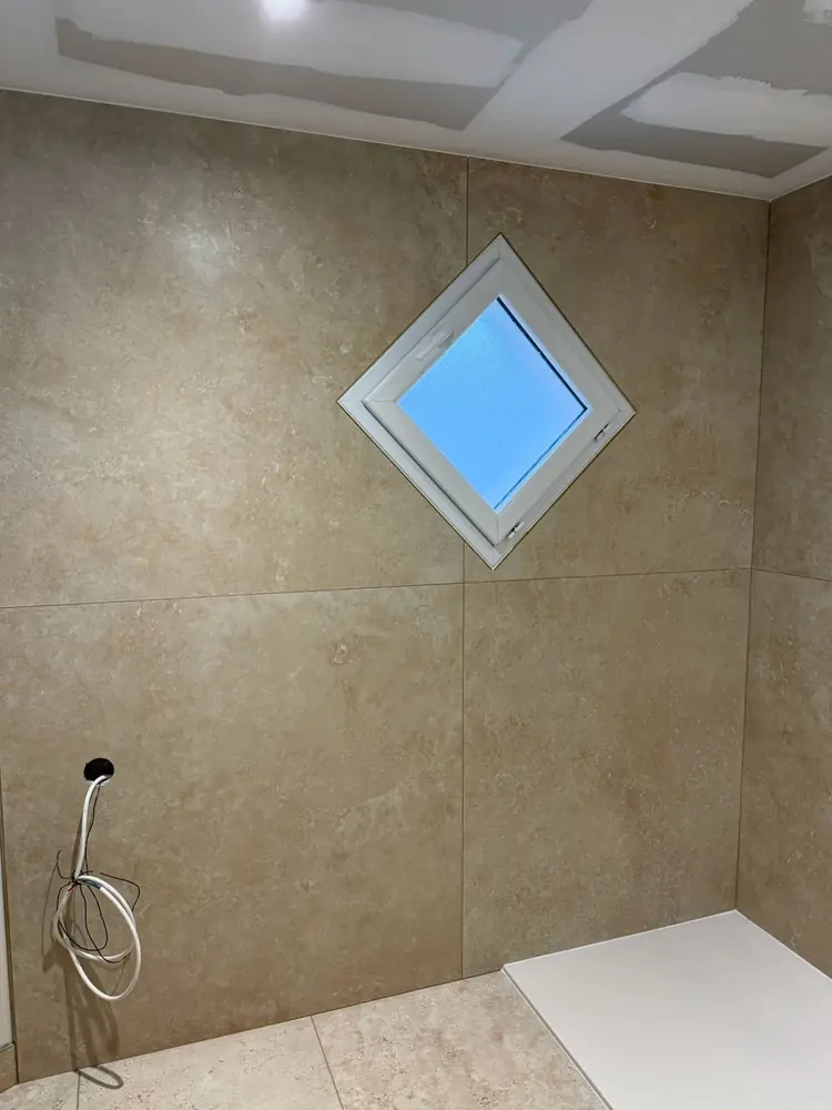 Mur en carrelage grand format effet pierre beige avec découpe précise autour d'une fenêtre en losange