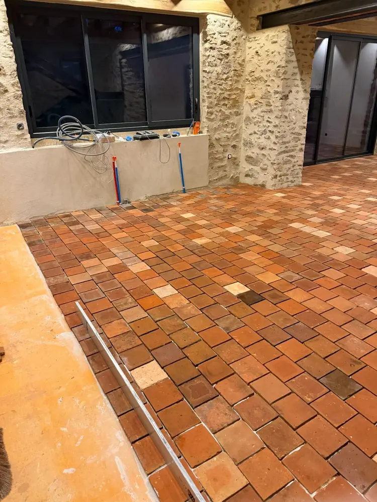 Pose de tomettes en terre cuite en cours, règle alu et support nu visibles au bord