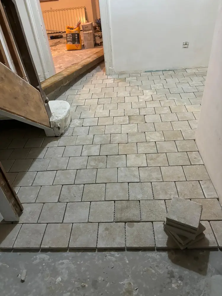 Pose en cours de travertin petit format au pied d'un escalier, carreaux en attente sur la chape