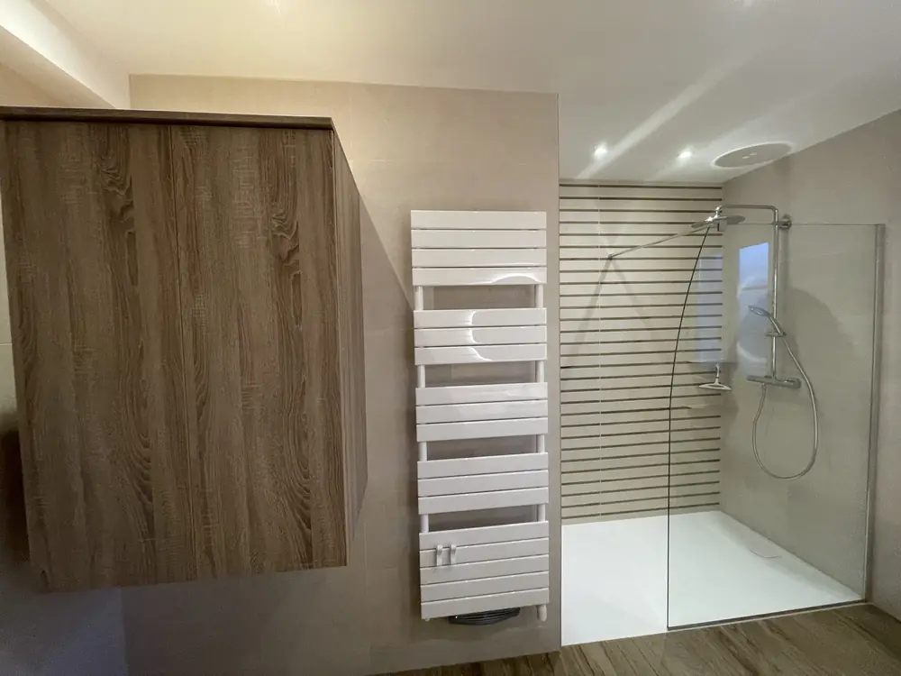 Salle de bain terminée avec douche à l'italienne, sèche-serviettes et meuble en bois