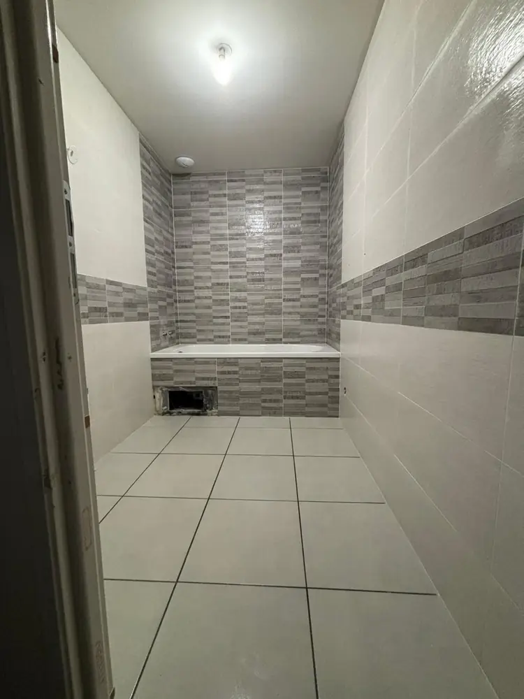 Salle de bain en faïence blanche avec frise et fond de baignoire en mosaïque grise