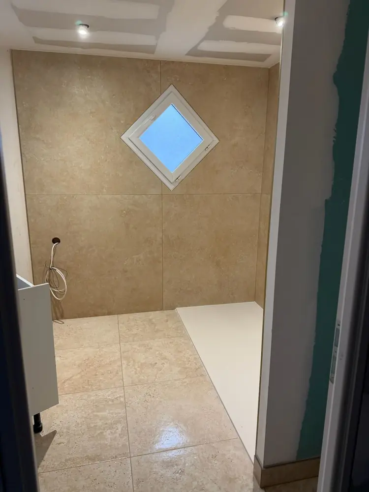 Salle de bain en grès cérame grand format effet pierre beige, murs et sol, fenêtre en losange
