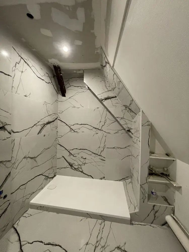 Salle d'eau sous rampant en grand format effet marbre blanc veiné noir, receveur et niches