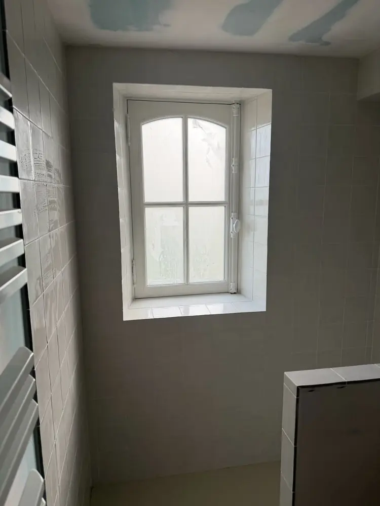 Salle d'eau en faïence blanche brillante avec fenêtre cintrée et muret de douche