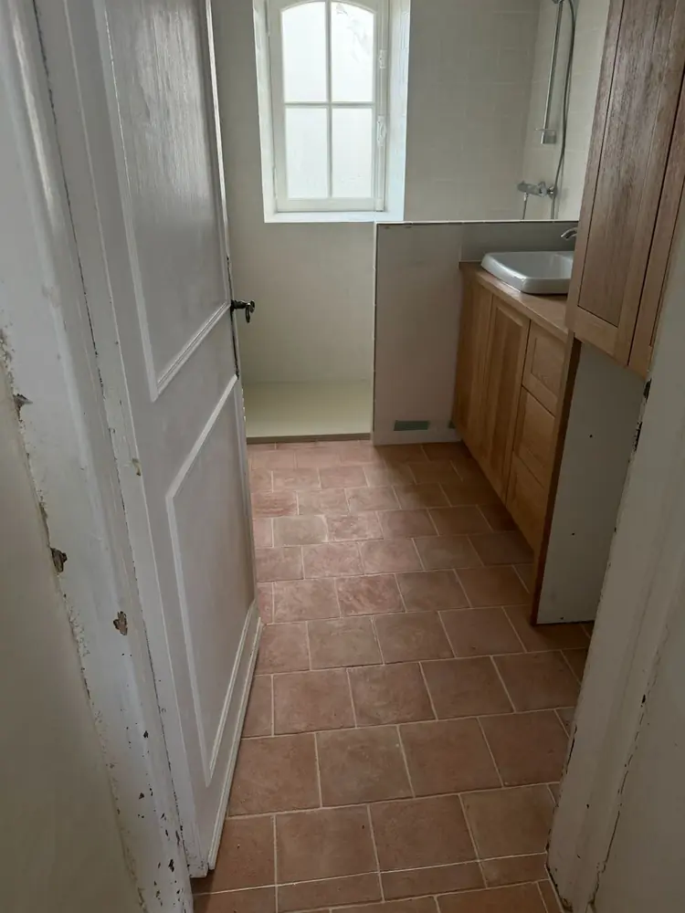 Salle d'eau avec sol en carreaux aspect terre cuite, faïence blanche et meuble vasque en bois