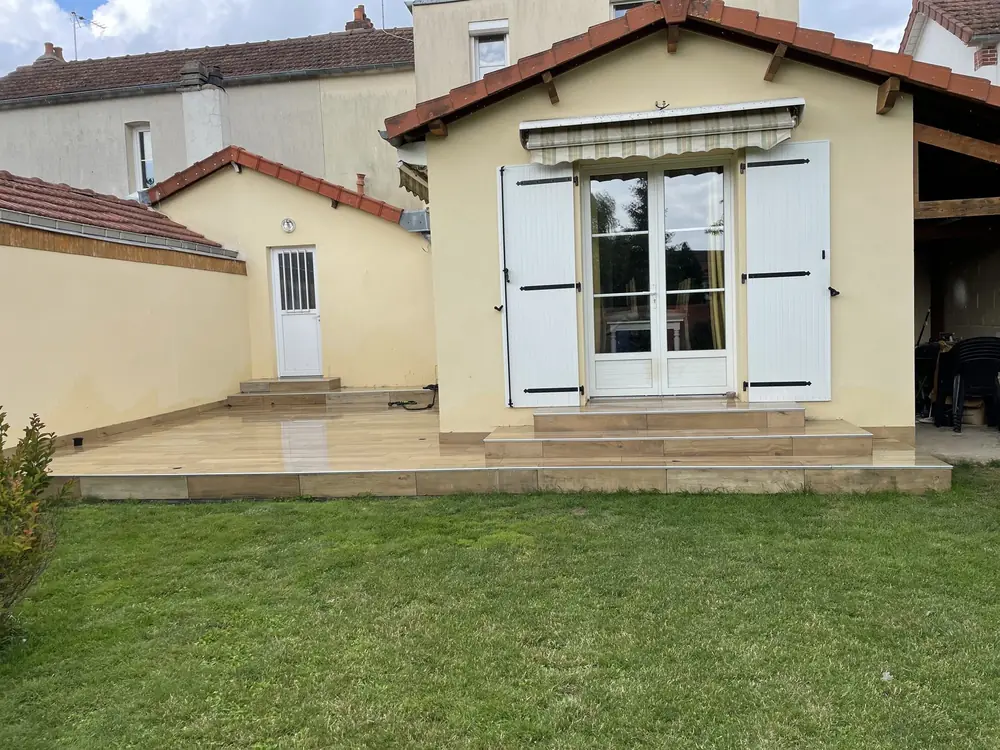 Terrasse surélevée et marches en carrelage imitation bois devant une maison aux volets blancs