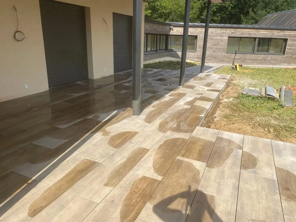 Terrasse couverte en carrelage imitation bois posée sous un auvent à poteaux acier